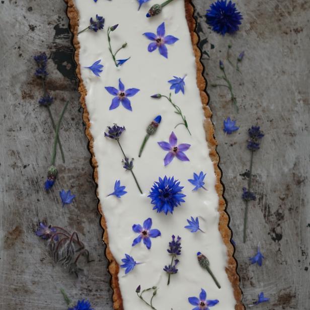 Eine rechteckige Tarte mit weißer Creme und blauen Blüten auf einem Backblech.