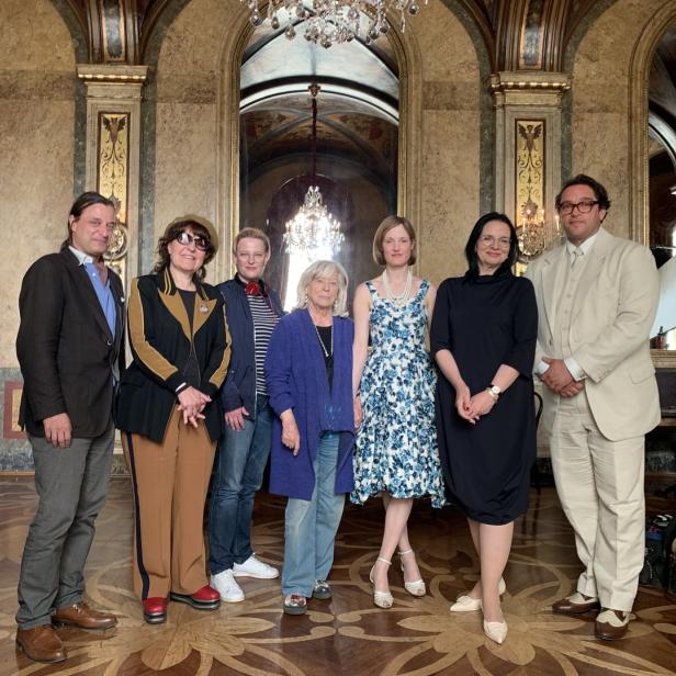 Eine Gruppe von sieben Personen posiert in einem opulenten Saal für ein Foto.