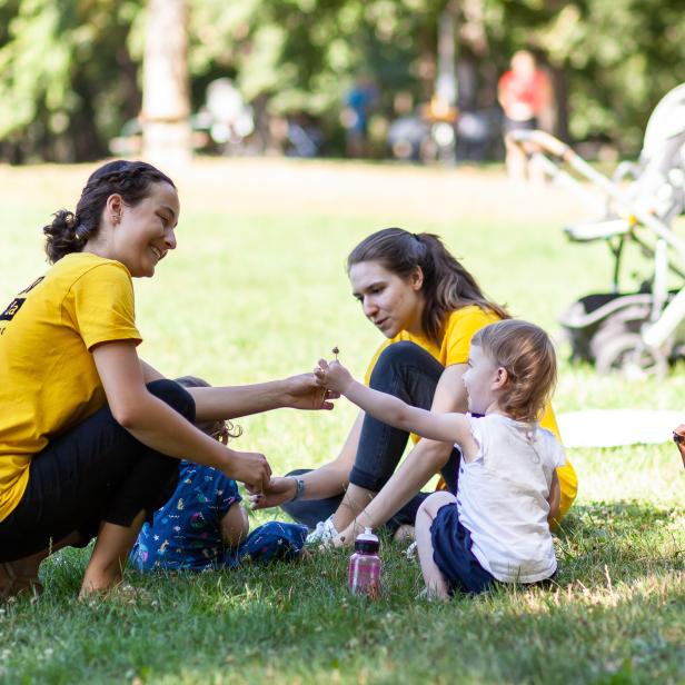 Zwei Frauen und zwei Kinder sitzen im Park auf einer Wiese.
