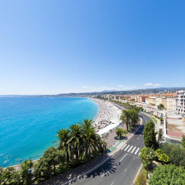 Ein Panoramablick auf die Küste von Nizza mit Strand, Palmen und Gebäuden.
