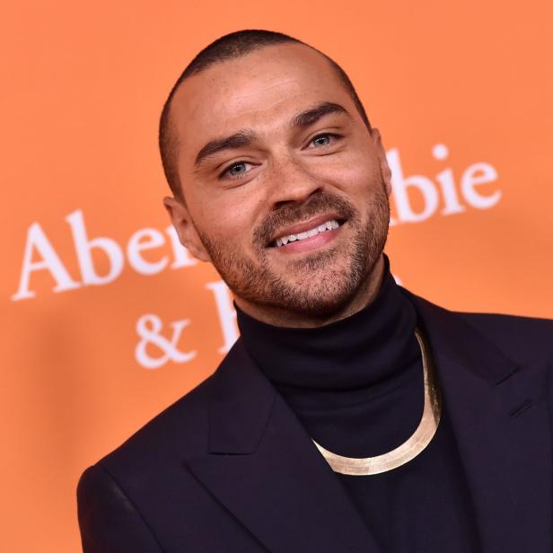 Jesse Williams lächelt vor einem orangefarbenen Hintergrund.