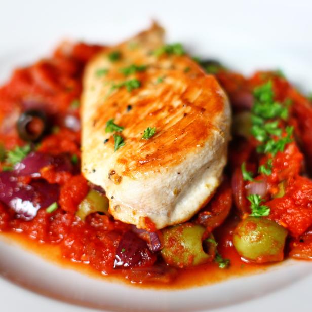 Ein Teller mit Hähnchenbrust in Tomatensauce mit Oliven und Zwiebeln.