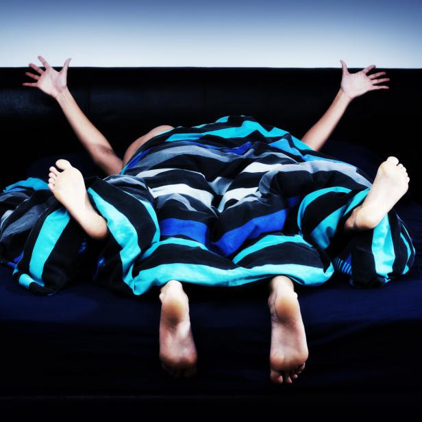 Zwei Personen liegen unter einer blau-schwarz gestreiften Decke im Bett.