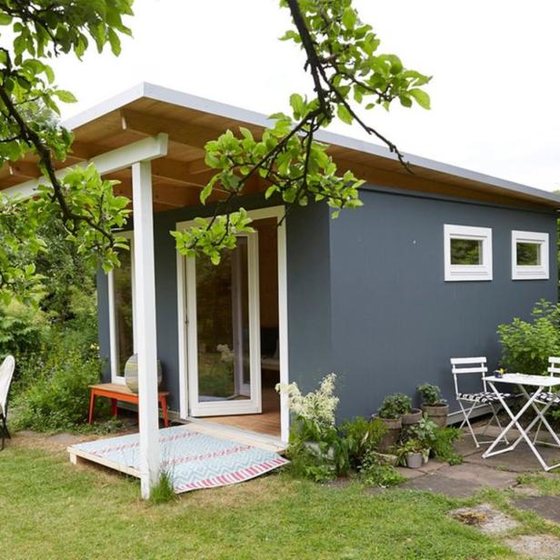 Ein graues Gartenhaus mit weißen Akzenten und einer kleinen Terrasse im Grünen.