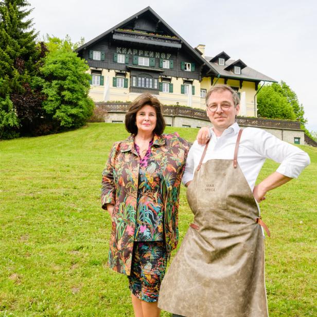Eine Frau in einem bunten Outfit und ein Koch mit Schürze stehen vor dem KnappenHof.