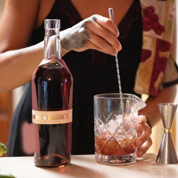 Eine Frau mit Tätowierung rührt einen Cocktail in einem Glas mit Eis.