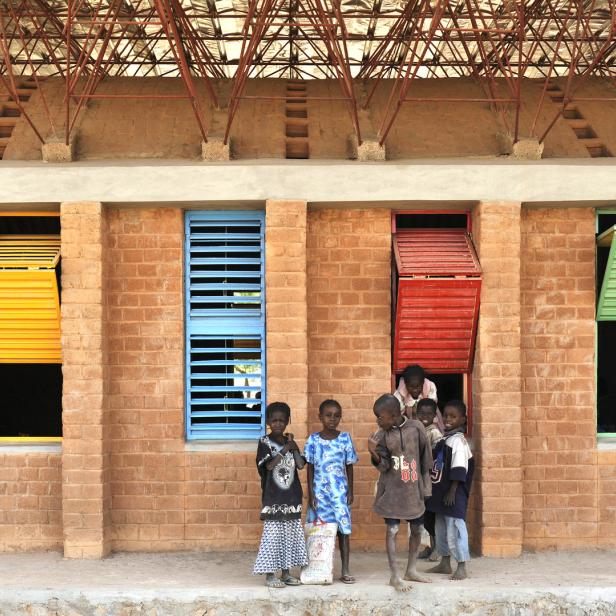 Eine Gruppe Kinder steht vor einem Backsteingebäude mit farbigen Fensterläden.