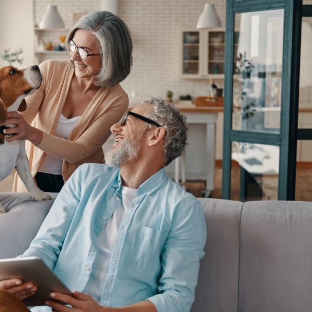 Ein älteres Paar kuschelt mit seinem Beagle auf dem Sofa, während der Mann ein Tablet benutzt.