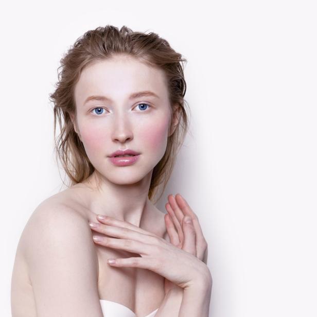 Eine junge Frau mit heller Haut und blauen Augen posiert vor einem weißen Hintergrund.