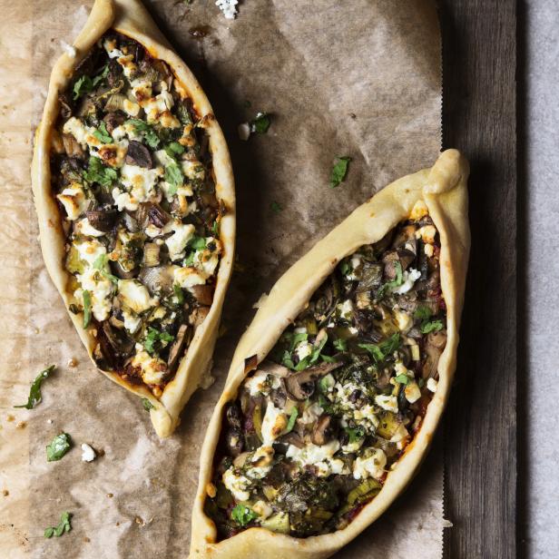 Zwei türkische Pide mit Gemüse und Feta auf Backpapier und Holzbrett.