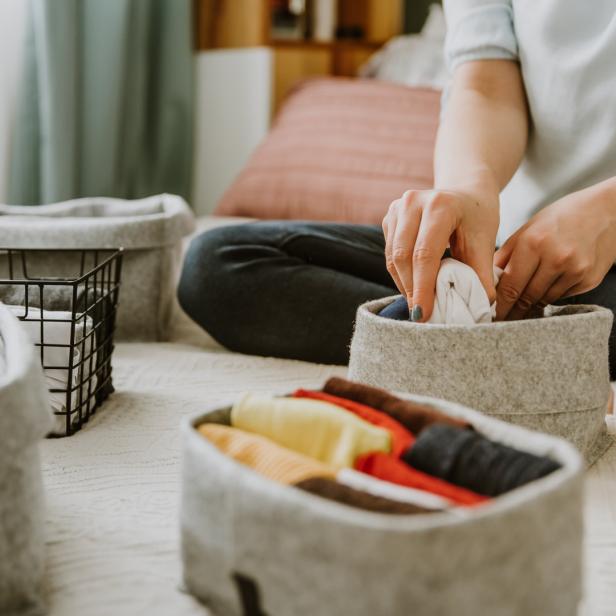 Eine Person faltet Kleidung und ordnet sie in Körben auf einem Bett an.