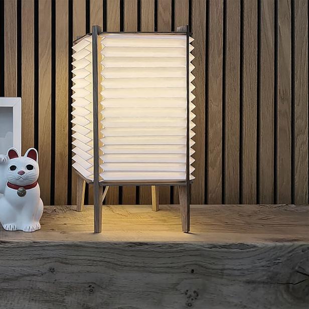Eine Maneki-Neko-Glückskatze steht neben einem gerahmten Handabdruck und einer Lampe auf einem Holzregal.