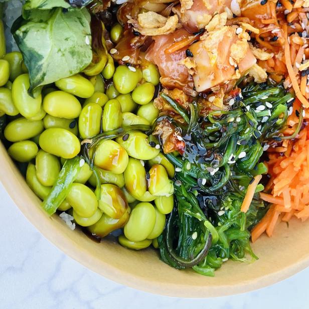 Eine Schüssel mit Edamame, Algensalat, Karotten und mariniertem Fisch.