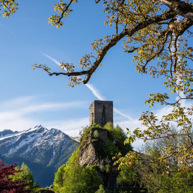 Ein mittelalterlicher Turm thront auf einem Felsen vor schneebedeckten Bergen.