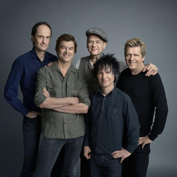 Die deutsche Rockband Die Ärzte posiert vor einem grauen Hintergrund.