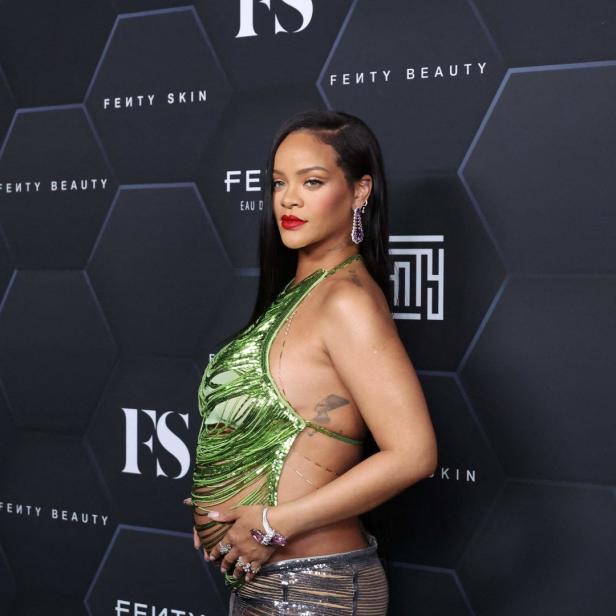 Rihanna posiert mit Babybauch vor einer Wand mit Fenty Beauty Werbung.