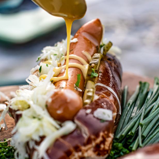 Senf wird auf einen Hotdog mit Wurst, Kraut und Gurken gegeben.