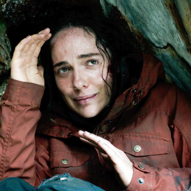 Eine Frau mit schmutzigem Gesicht und Jacke kauert in einer Felsspalte.