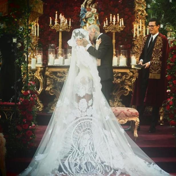 Travis Barker und Kourtney Kardashian bei ihrer Hochzeit, umgeben von Kerzen und roten Rosen.