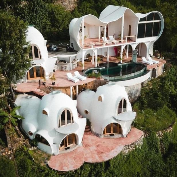 Ein ungewöhnliches, weißes Haus mit Kuppeln und einem Pool liegt auf einem grünen Hügel.