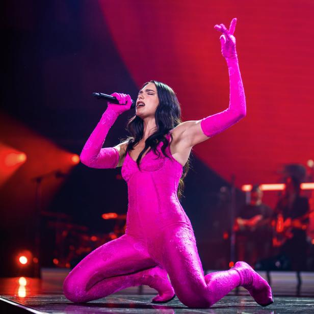Dua Lipa kniet auf der Bühne und singt in einem pinkfarbenen Outfit.