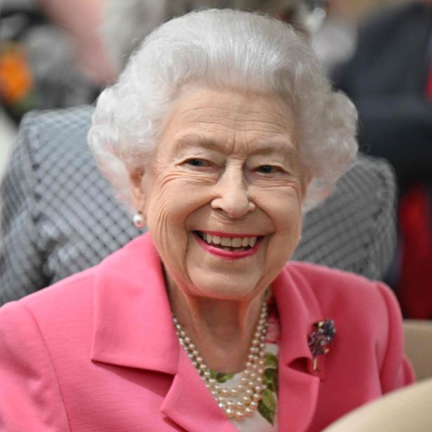 Königin Elizabeth II. lächelt in einem pinkfarbenen Blazer und einer Perlenkette.