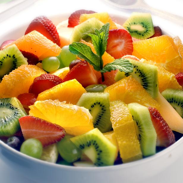 Ein Teller mit frischem Obstsalat, bestehend aus Erdbeeren, Kiwi, Orangen und Weintrauben.