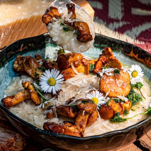 Ein Teller Risotto mit Pfifferlingen, Parmesan und Gänseblümchen wird mit einem Löffel serviert.