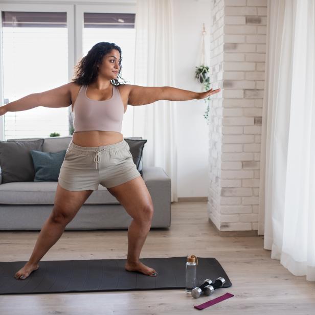 Eine Frau macht Yoga auf einer Matte in einem hellen Wohnzimmer.