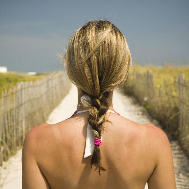Eine Frau mit blonden Haaren geht einen Weg am Strand entlang.