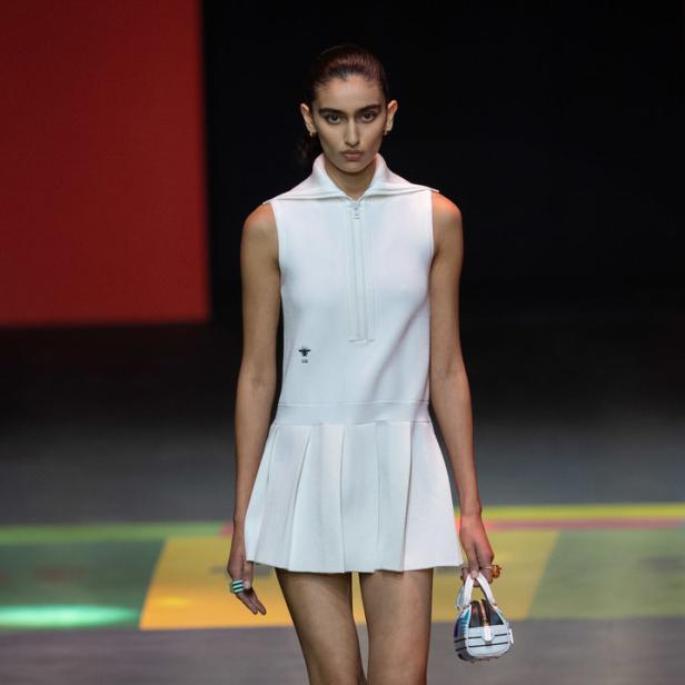 Eine Frau in einem weißen Dior-Kleid mit Faltenrock und passenden Stiefeln auf dem Laufsteg.