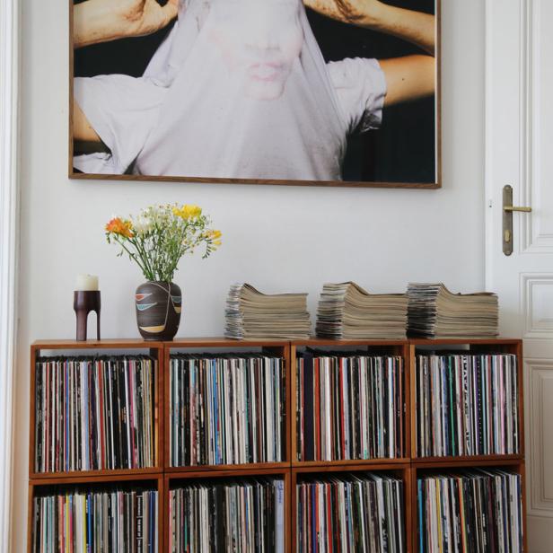 Ein Regal voller Schallplatten und Zeitschriften unter einem gerahmten Porträt an einer weißen Wand.