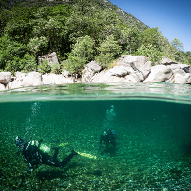 Zwei Taucher erkunden einen Fluss mit klarem, grünem Wasser.
