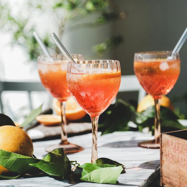 Drei Gläser Aperol Spritz mit Eis und Orangenscheiben auf einem Tisch mit Zitrusfrüchten.