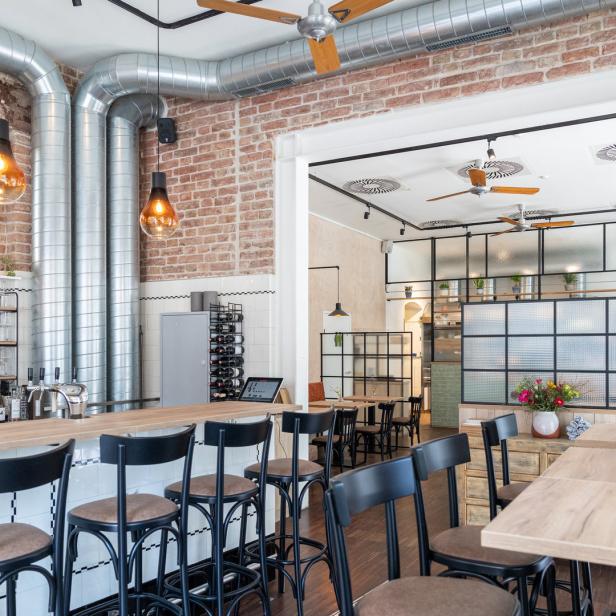 Innenansicht eines hellen Restaurants mit Bar, Tischen und Stühlen.