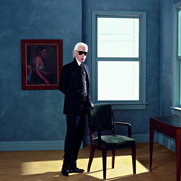 Karl Lagerfeld posiert in einem dunklen Anzug und Sonnenbrille in einem blauen Raum.