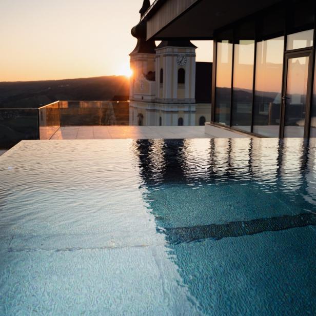 Ein Infinity-Pool spiegelt eine Kirche bei Sonnenuntergang wider.