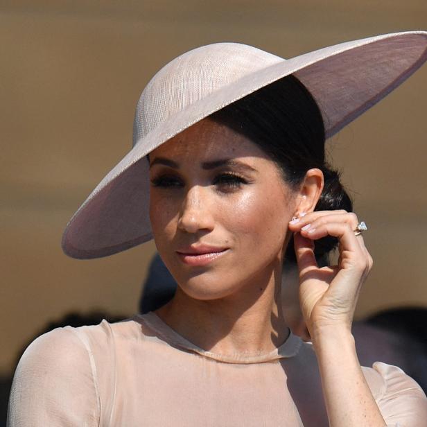 Meghan, Herzogin von Sussex, mit einem hellen Hut, berührt ihr Ohr.