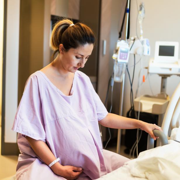 Eine schwangere Frau sitzt in einem Krankenhausbett.
