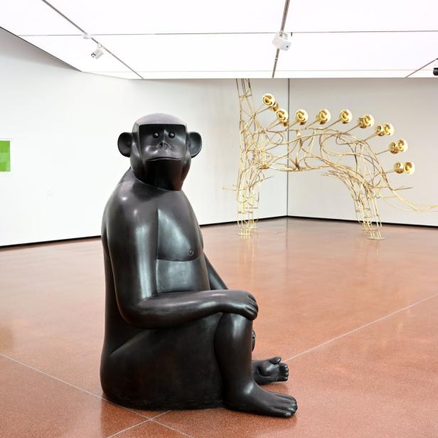 Eine dunkle Affenskulptur sitzt in einer Kunstgalerie.