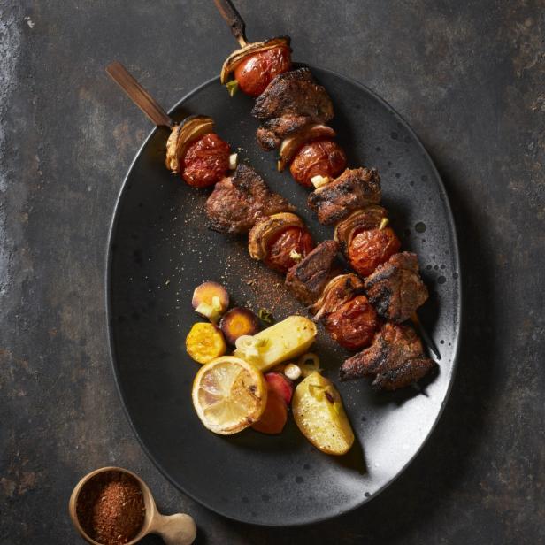 Zwei Spieße mit gegrilltem Fleisch, Tomaten und Zwiebeln auf einem Teller mit Gemüsebeilage.