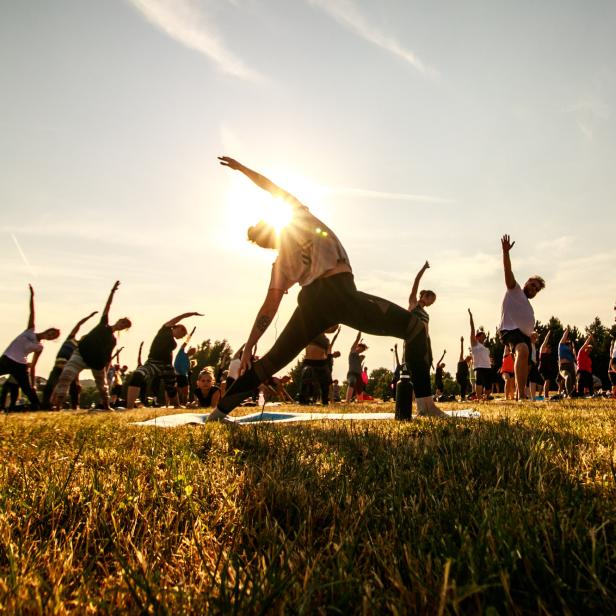 Eine Gruppe von Menschen praktiziert Yoga im Freien bei Sonnenaufgang.