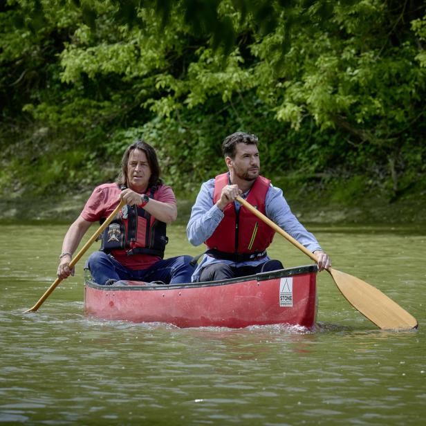Zwei Männer paddeln in einem roten Kanu auf einem Fluss.