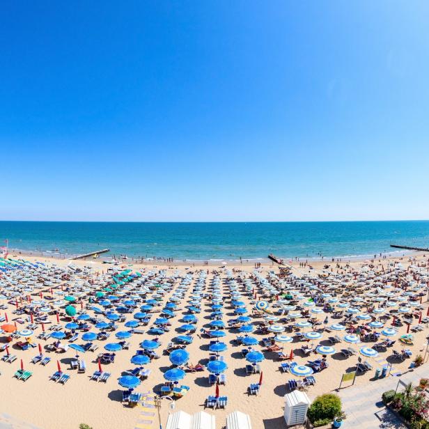 Ein weitläufiger Sandstrand mit unzähligen Sonnenschirmen unter einem strahlend blauen Himmel.