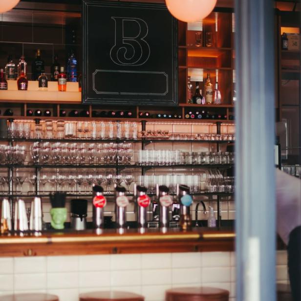 Eine Bar mit Hockern, Zapfhähnen und einer Tafel mit einem großen „B“.