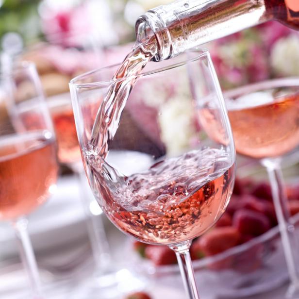 Roséwein wird in ein Glas gegossen, Erdbeeren und Blumen im Hintergrund.
