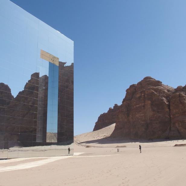 Ein verspiegeltes Gebäude steht in der Wüste und reflektiert die umliegenden Felsen.