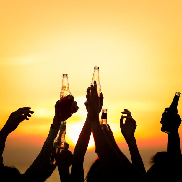 Menschen stoßen bei Sonnenuntergang mit Bierflaschen an.