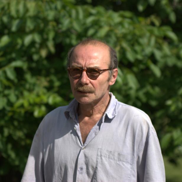 Ein Mann mit Schnurrbart und Brille vor einem grünen Hintergrund.