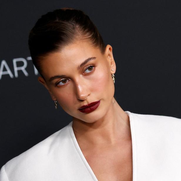 Hailey Bieber bei einer Veranstaltung mit dunklem Lippenstift und weißem Blazer.